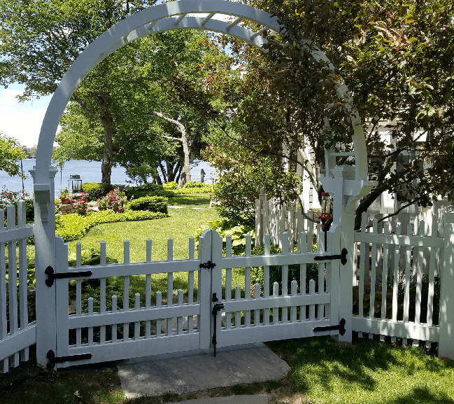 a white picket fence with a white gate, which is situated in a grassy area